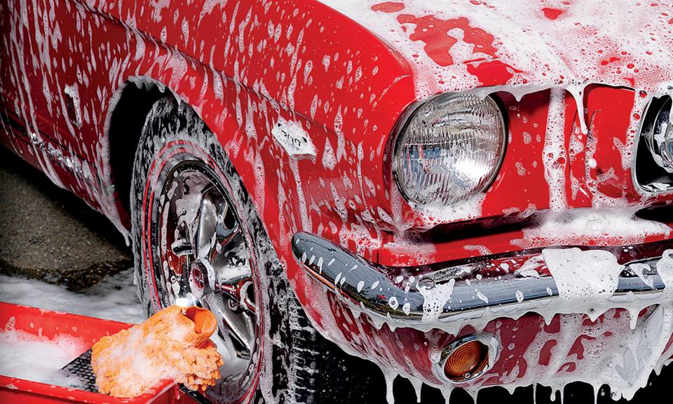 Red classic car being washed with soap and a sponge